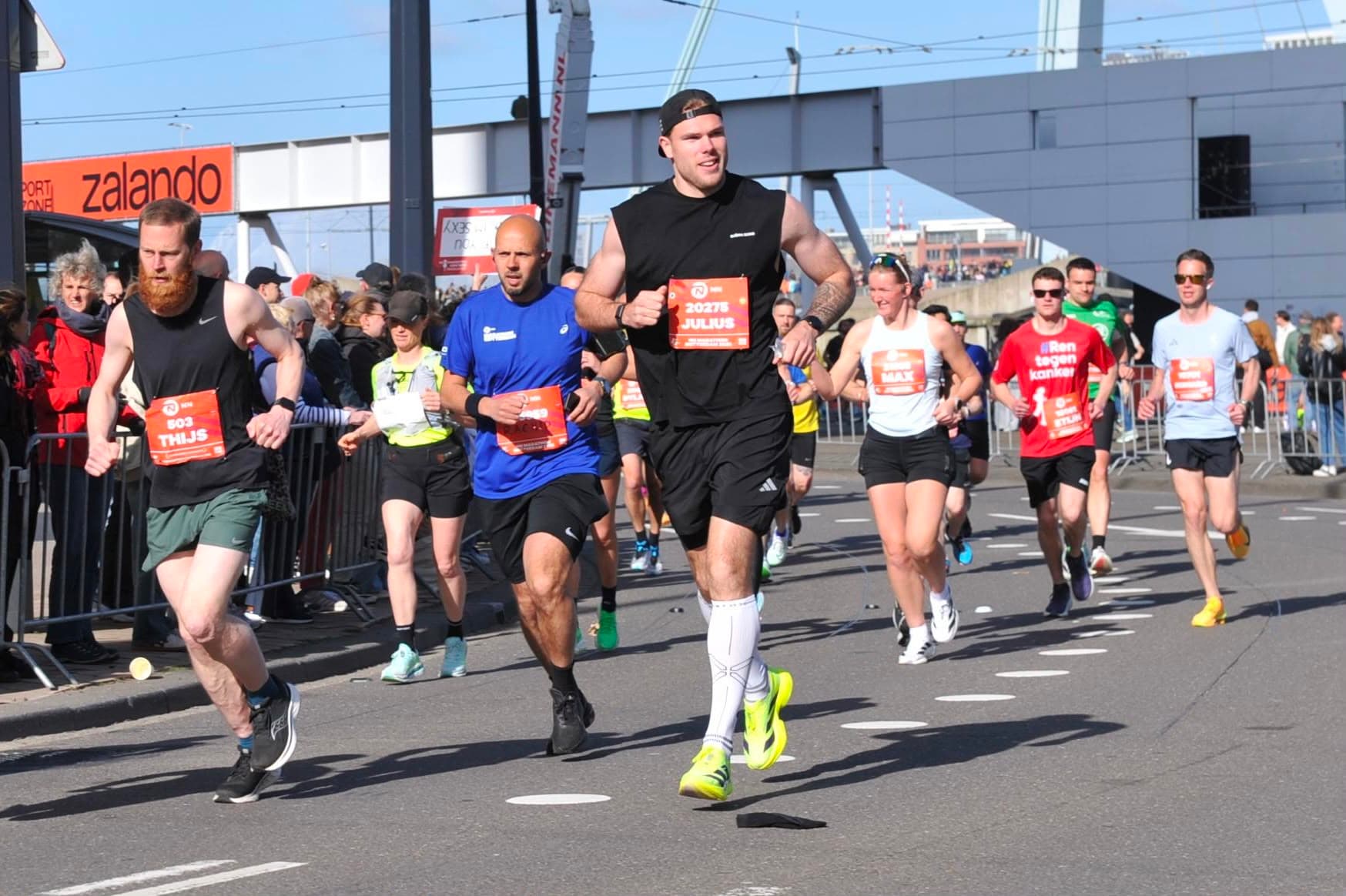 Julius Roters in volle vaart tijdens de NN Marathon Rotterdam, oranje startnummer 20275, voltgele hardloopschoenen